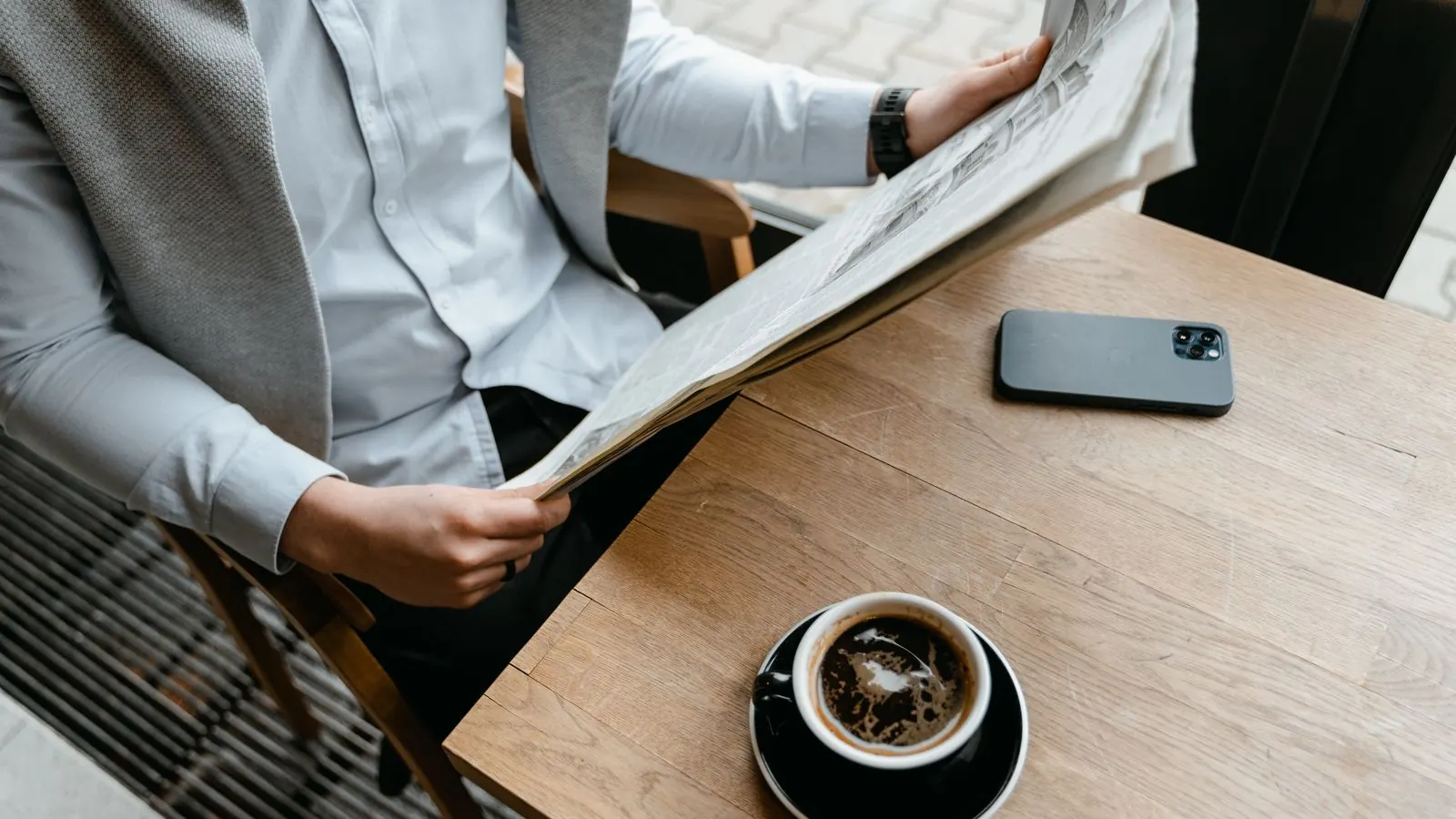 A man reading a newspaper over coffee in a cafe with his smartphone on the table