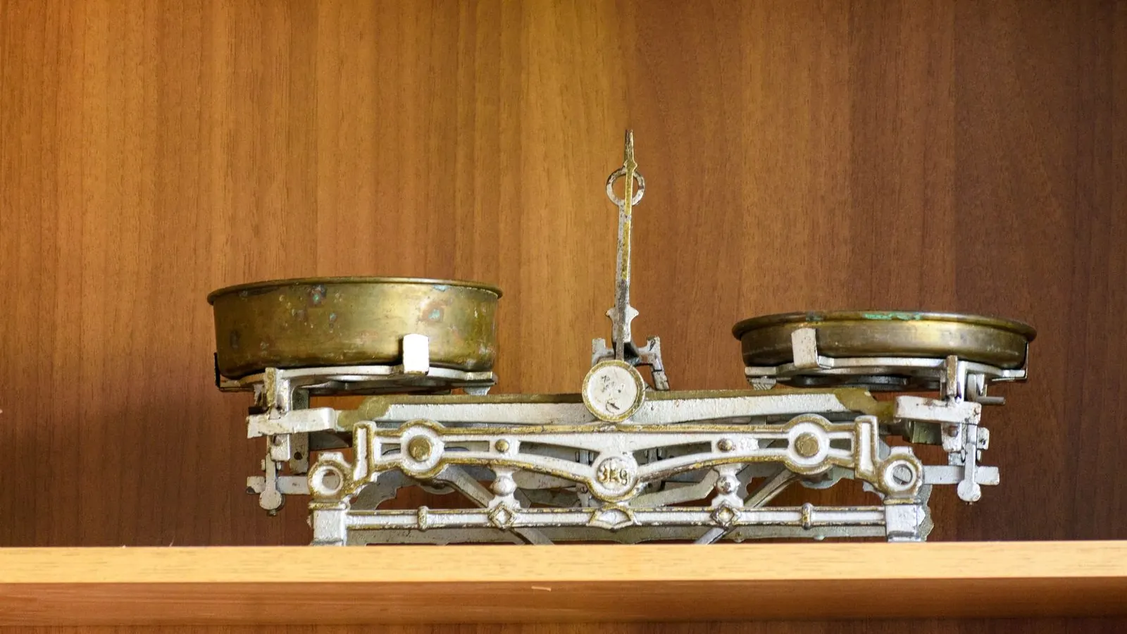 A vintage brass balance scale with two pans on a wooden shelf