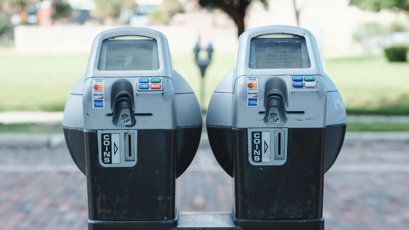 Two coin-and-card parking meters side by side on a brick pavement, each with a coins slot and a card reader
