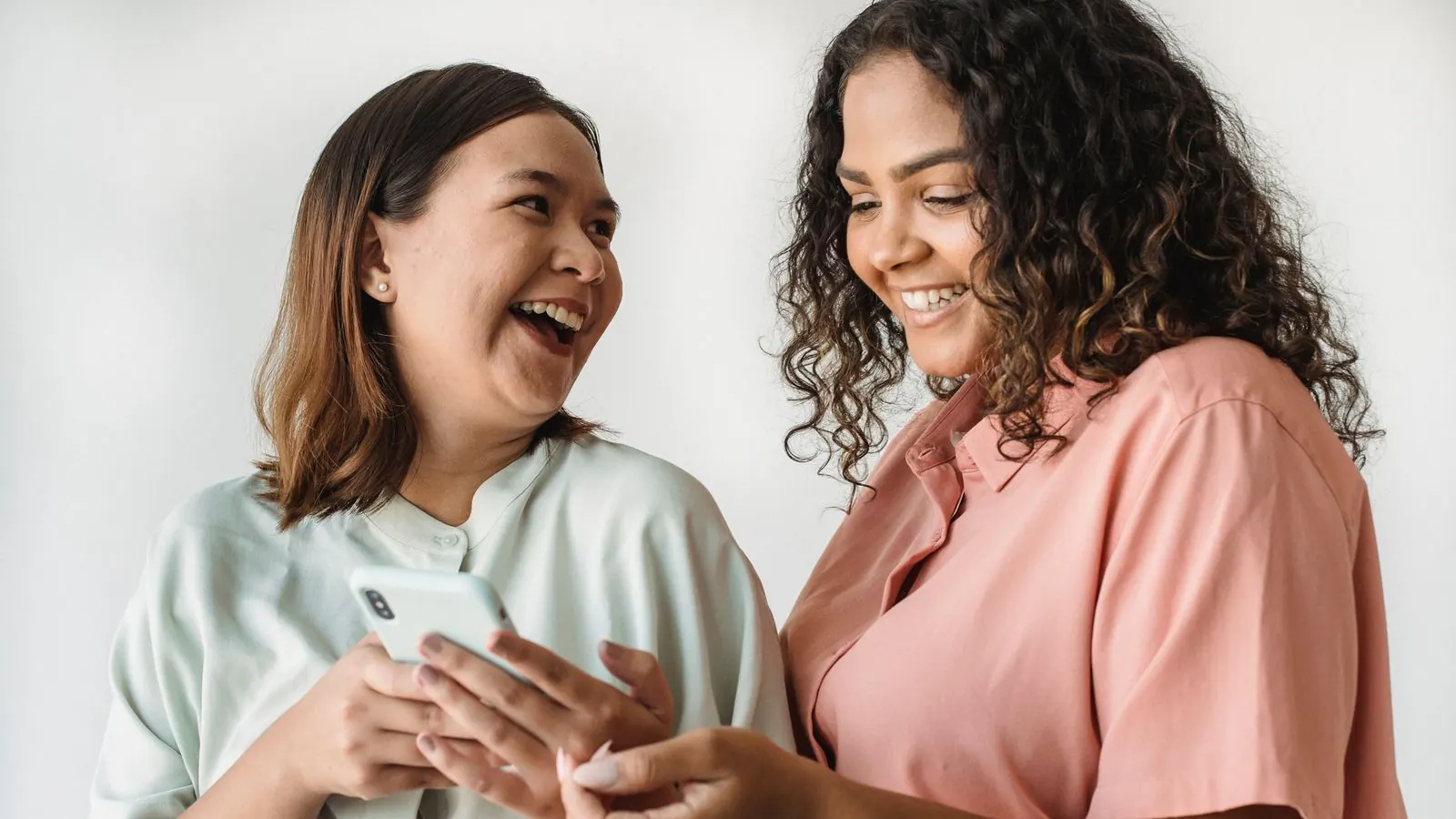 Two women laughing together while looking at a smartphone