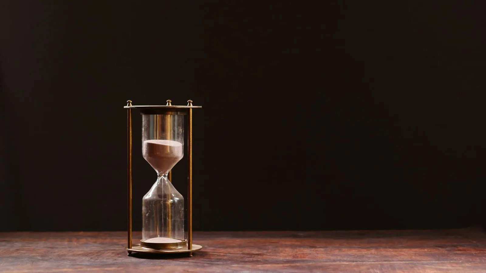An hourglass with sand running through it against a dark background