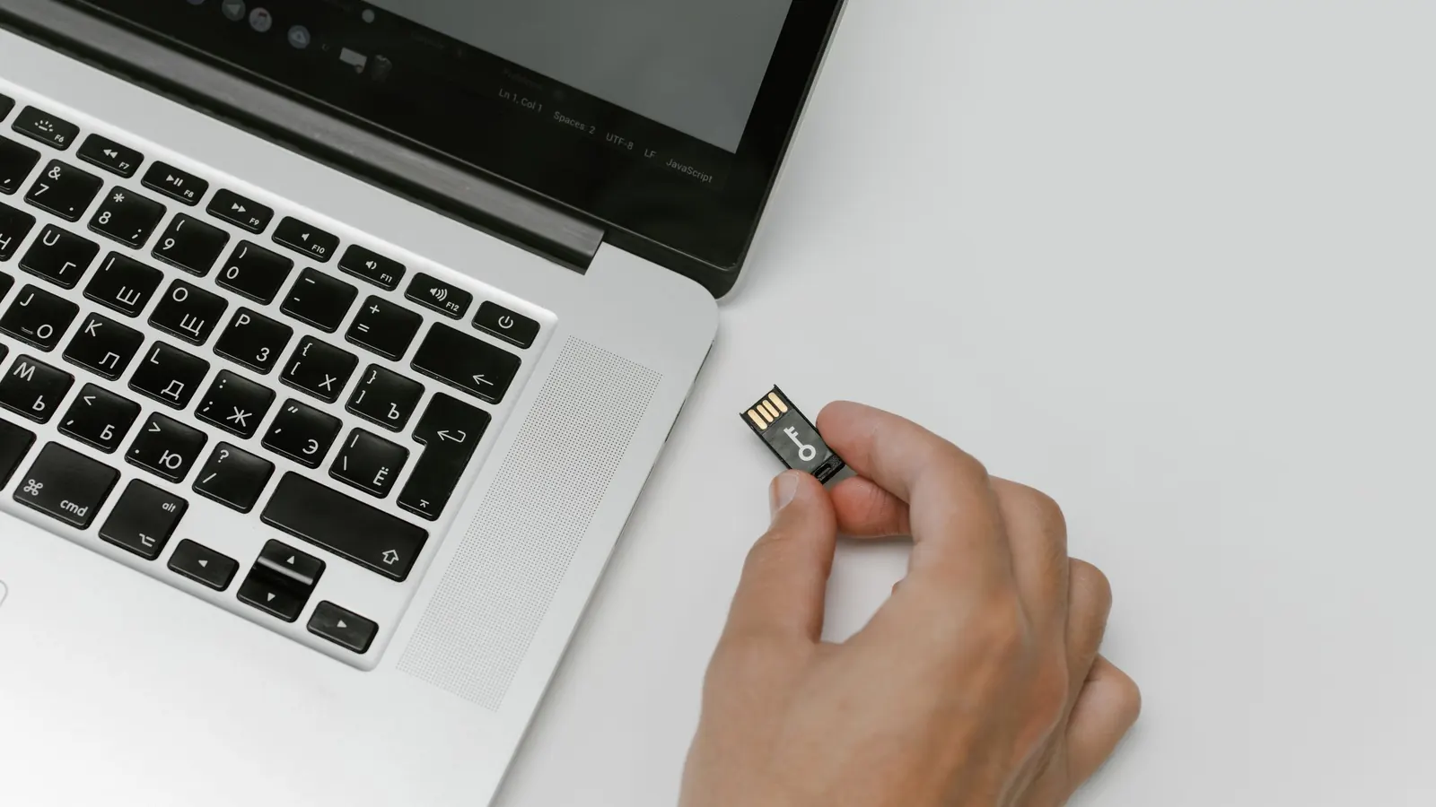 A hand holding a small USB flash drive beside a laptop keyboard