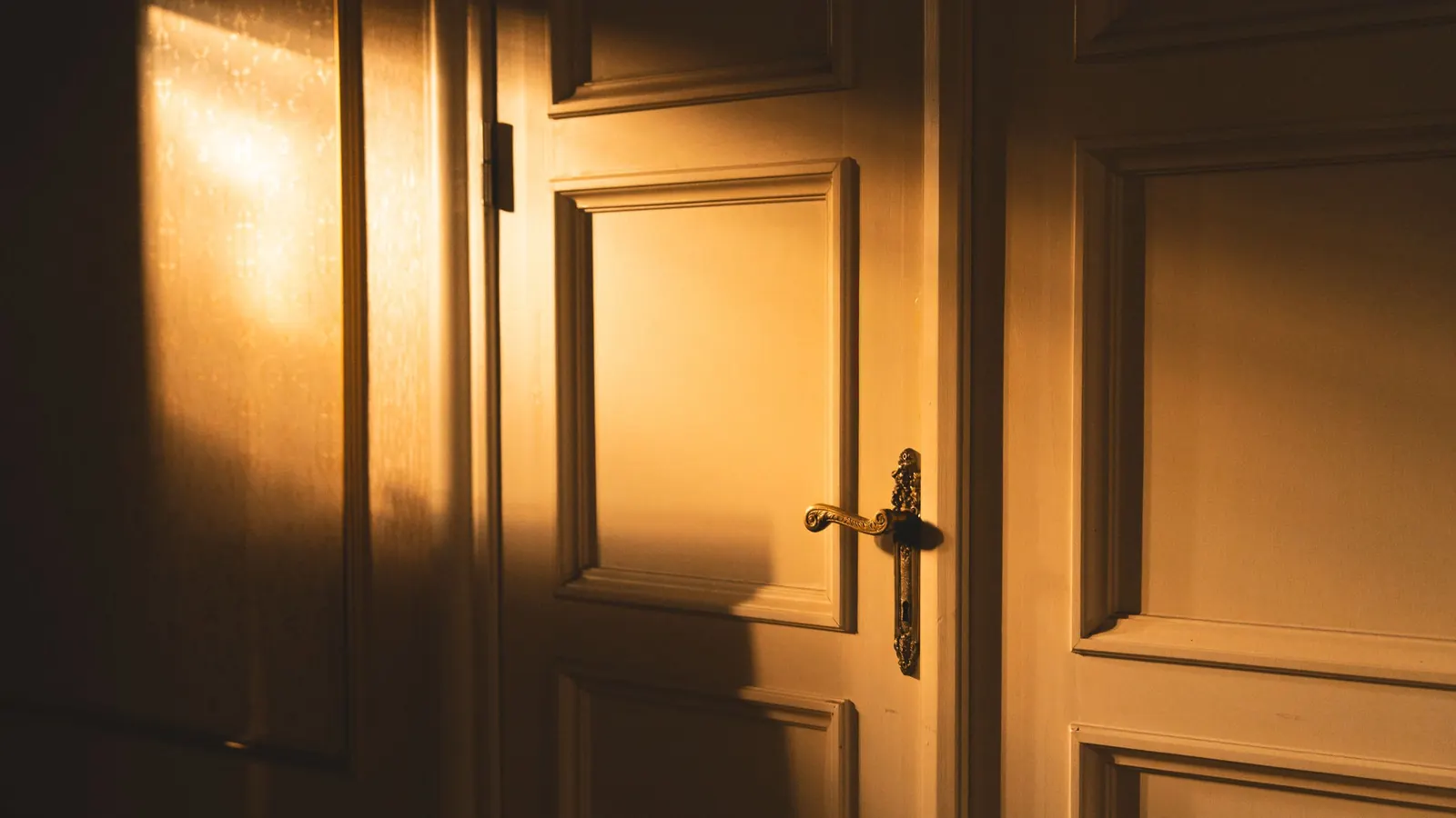 Warm evening sunlight falling across a white panelled door with a brass handle, standing partly open
