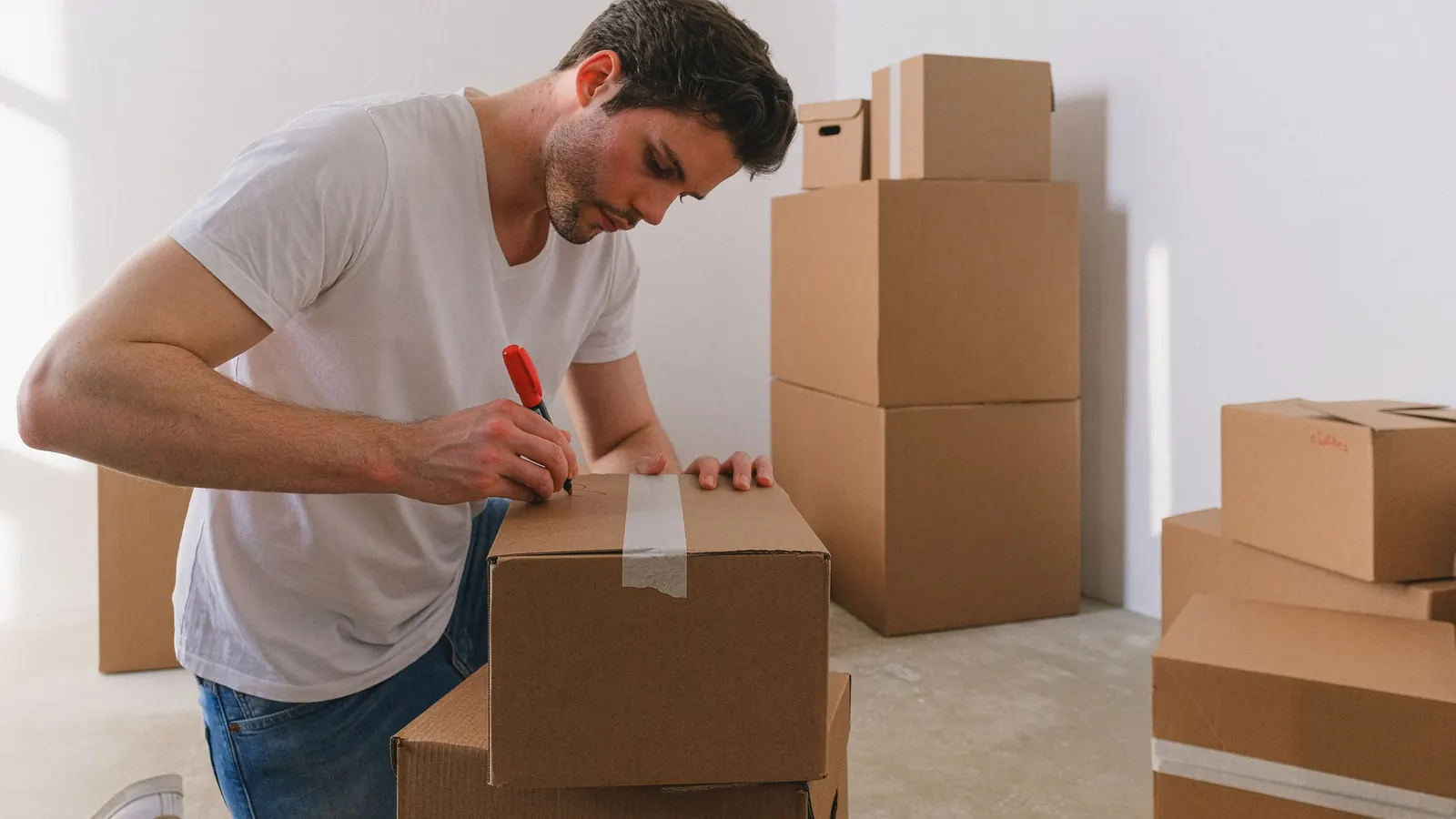 A man kneeling on the floor labelling cardboard moving boxes with a marker